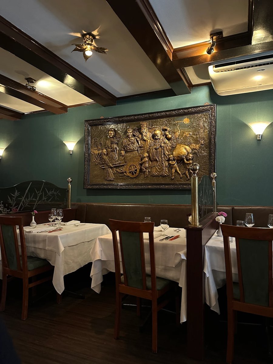De sfeervolle eetzaal van Sichuan Food met diepgroene wanden, brons reliëf en wit gedekte tafels